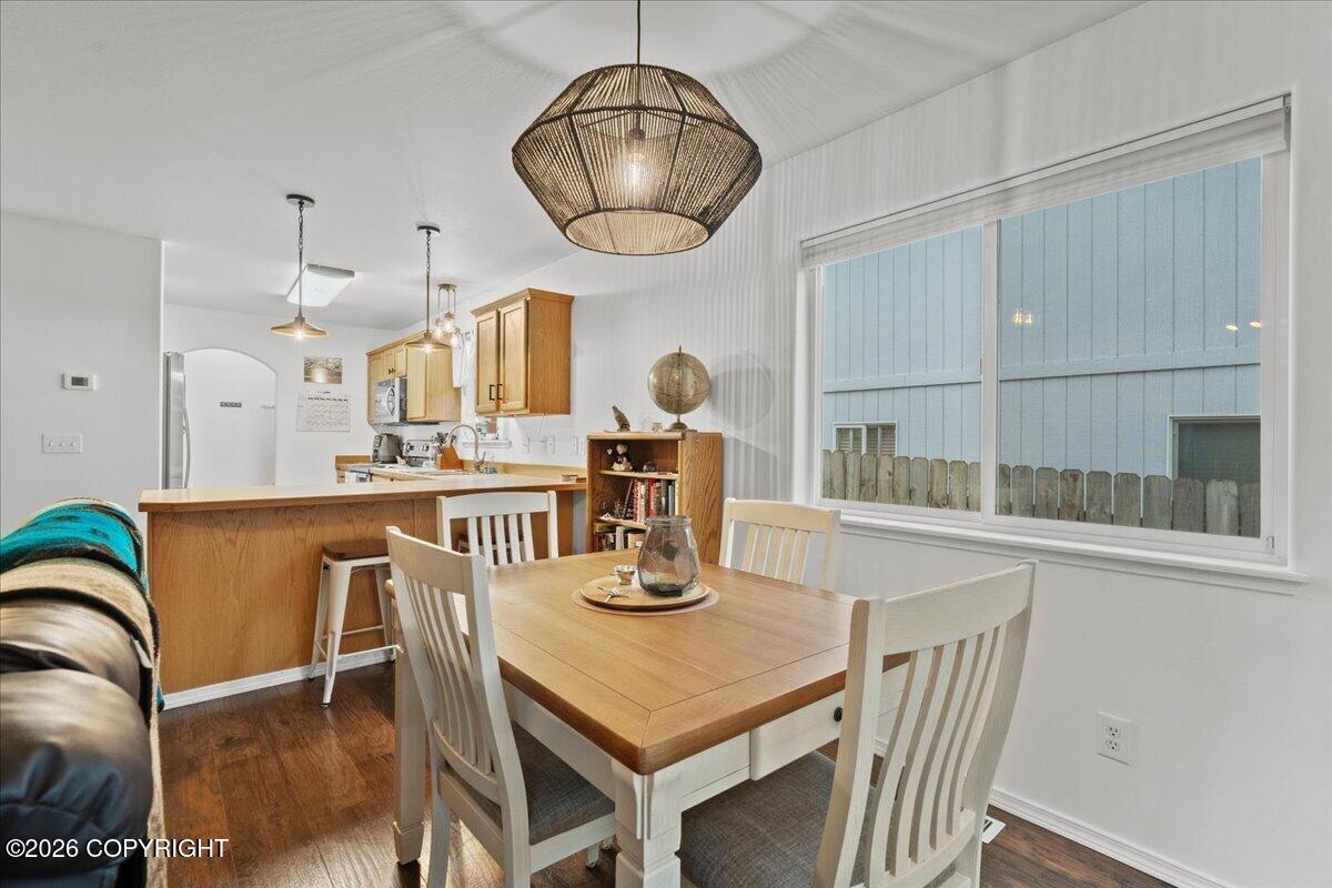 Dining area with a light wood table and white chairs beside an open kitchen and large window.
