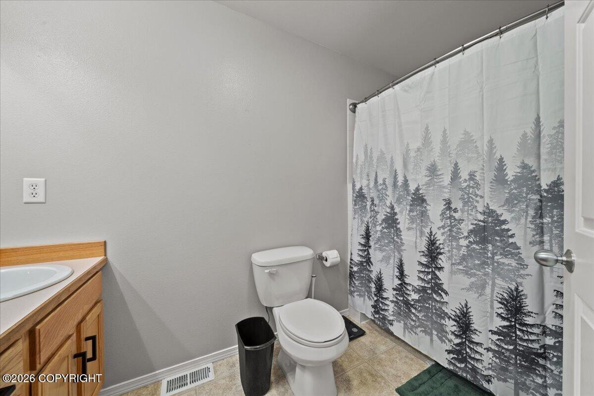 Bathroom with a wood vanity, toilet, and forest-print shower curtain.