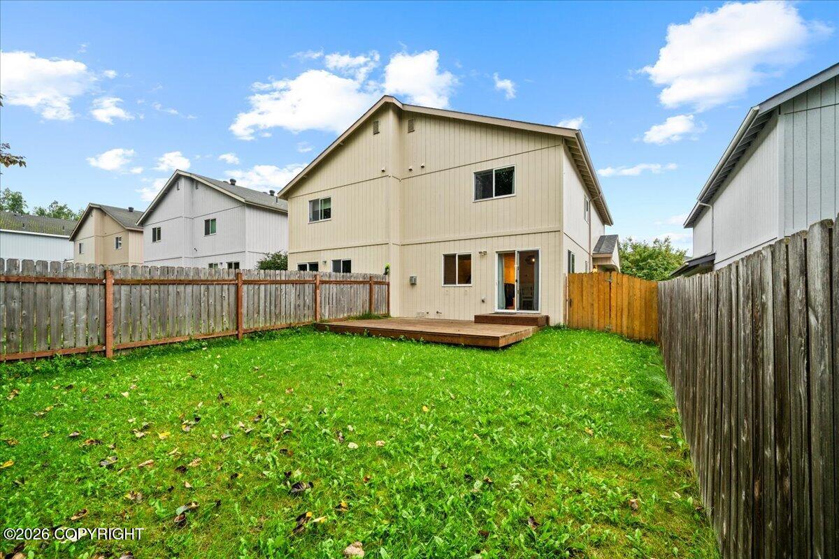 Two-story beige home behind a fenced grassy backyard, with a small wooden deck.