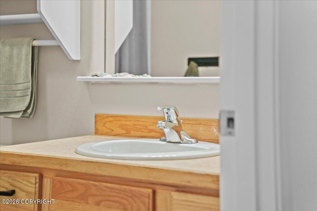 Bathroom vanity with an oval sink, chrome faucet, and light wood cabinet, partly viewed through a doorway.