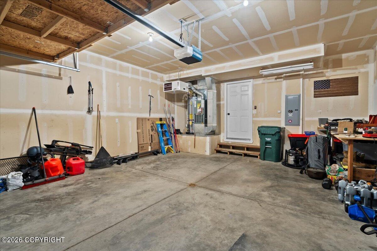 Garage with unfinished drywall, exposed ceiling joists, and a white entry door.
