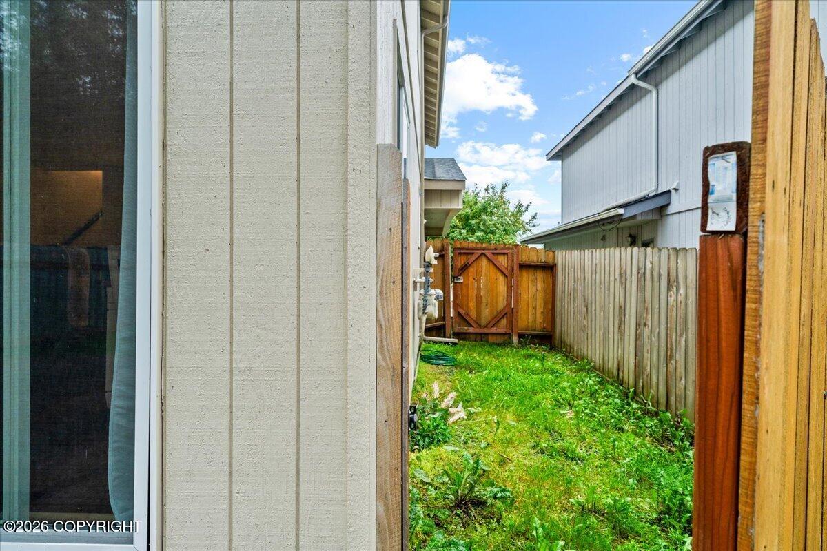 Fenced side yard with grass, a wooden gate, and a garden hose between neighboring homes.