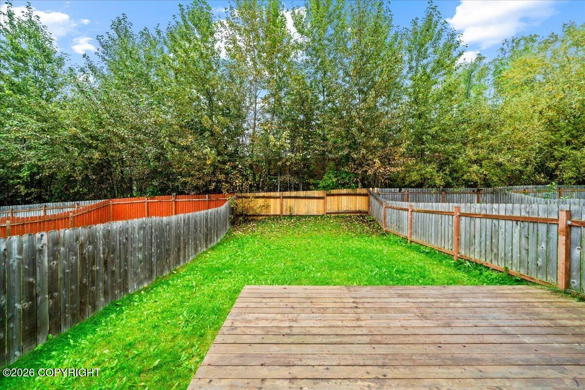 Fenced backyard with a wooden deck, green lawn, and mature trees.