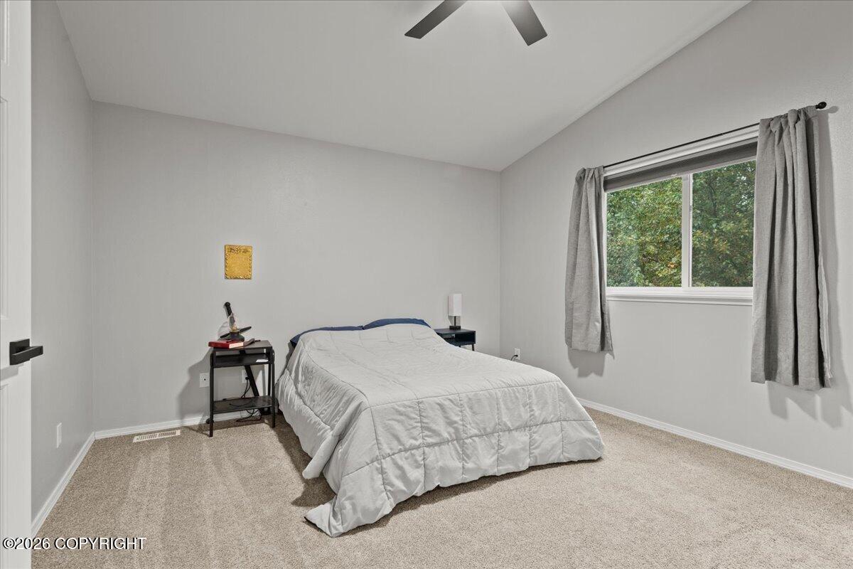 Furnished bedroom with a gray-quilted bed and a curtained window overlooking trees.