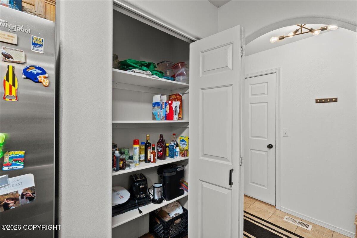 Stocked kitchen pantry with open shelving, small appliances, and an adjacent stainless steel refrigerator.