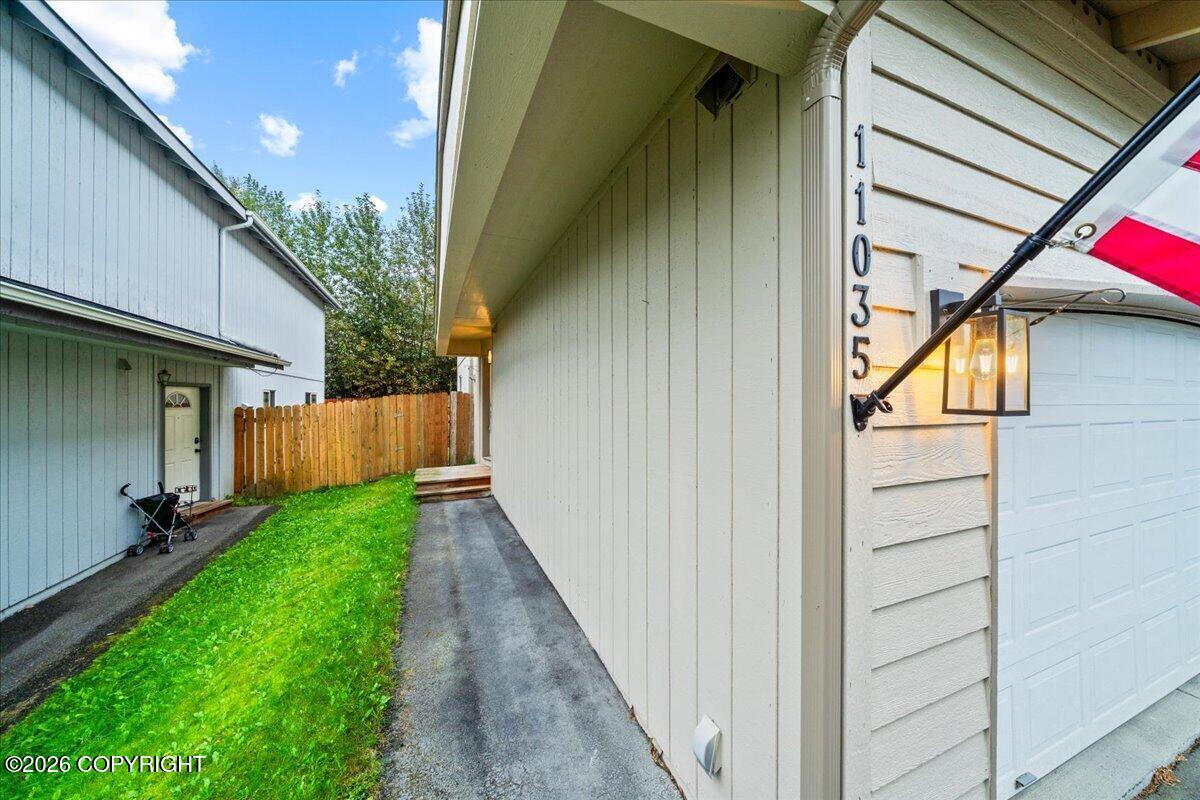 Home exterior with garage, American flag, and paved side path beside a green lawn.