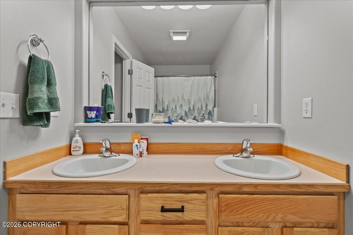 Bathroom vanity with double sinks, wood cabinetry, and a wide mirror reflecting a forest-patterned shower curtain.
