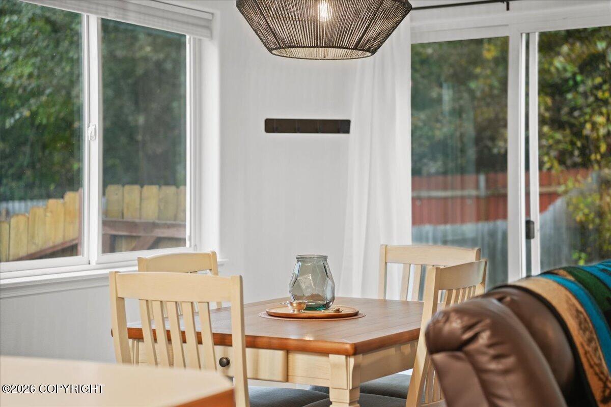 Dining area with a wooden table, woven pendant light, and large windows overlooking trees.