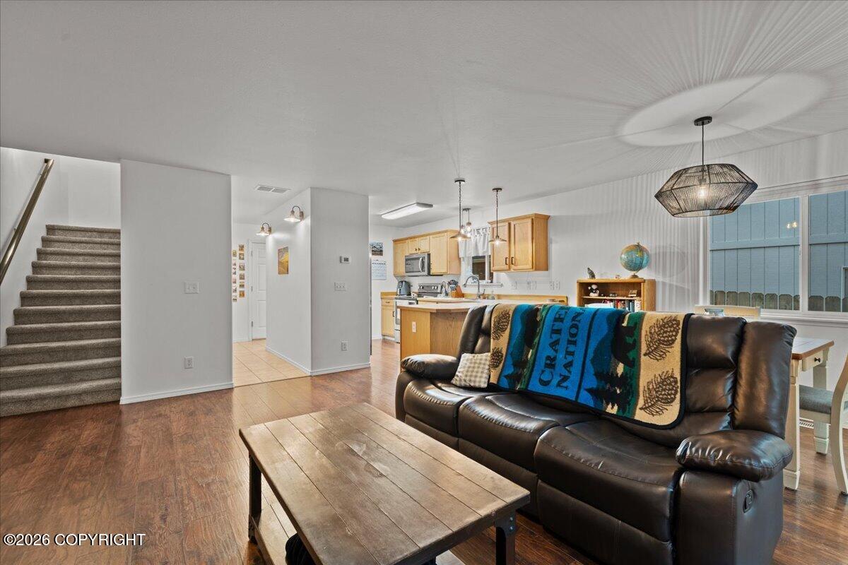 Open-plan living room with a dark leather sectional, wood coffee table, and kitchen beyond.