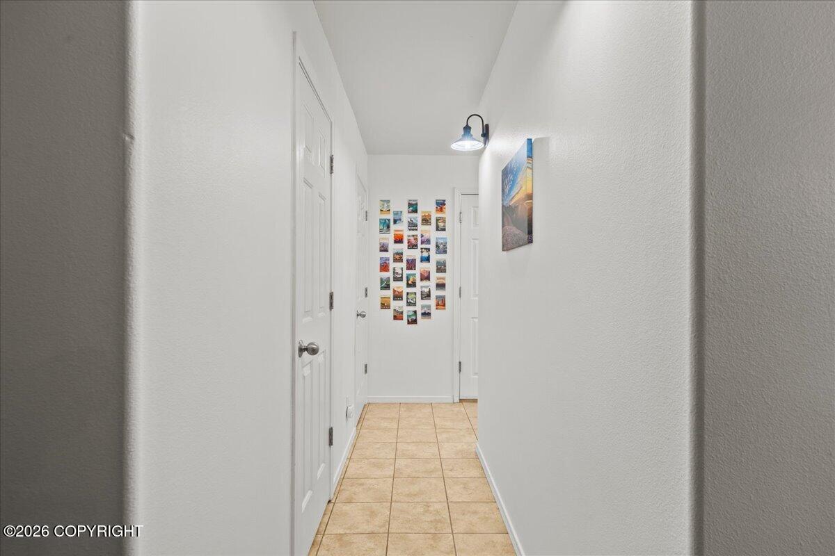 White hallway with tan tile floors, several doors, and colorful postcards displayed at the far end.