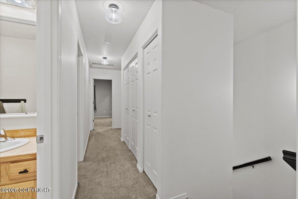 Carpeted hallway with white closet doors, a bathroom vanity, and a stair railing.