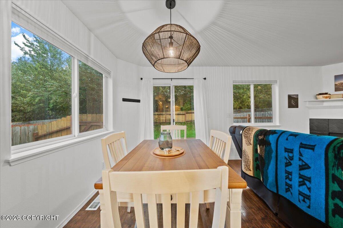Dining area with a wooden table, woven pendant light, and large windows overlooking a fenced yard.