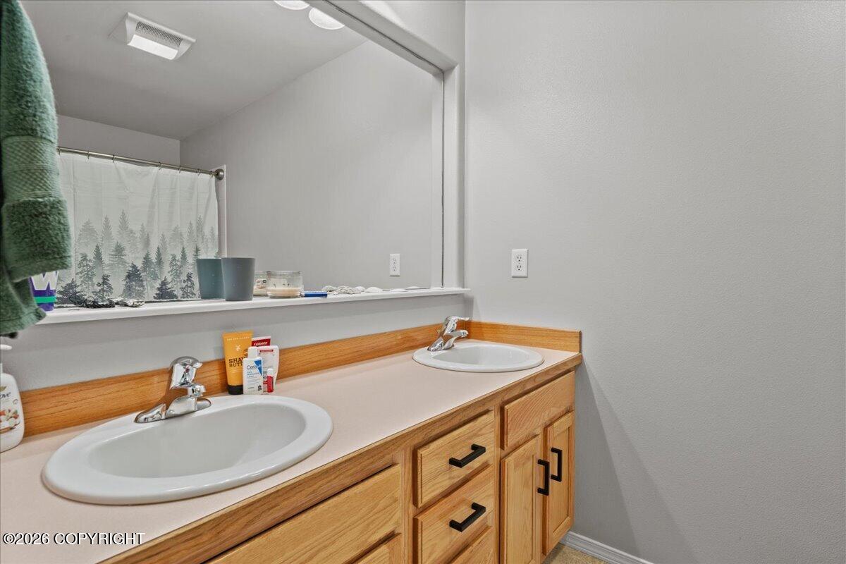 Bathroom vanity with double sinks, light wood cabinetry, and a tree-print shower curtain reflected in the mirror.