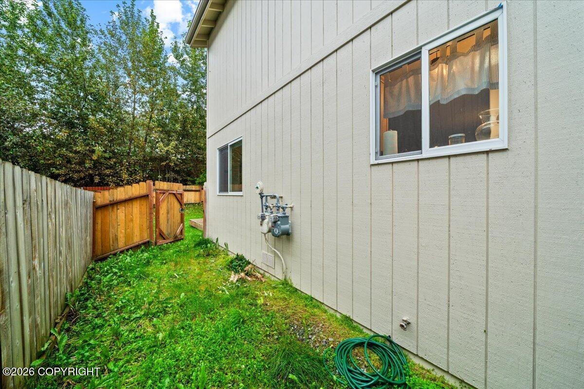 Residential building’s side yard with a wooden fence, utility meters, and a coiled garden hose.
