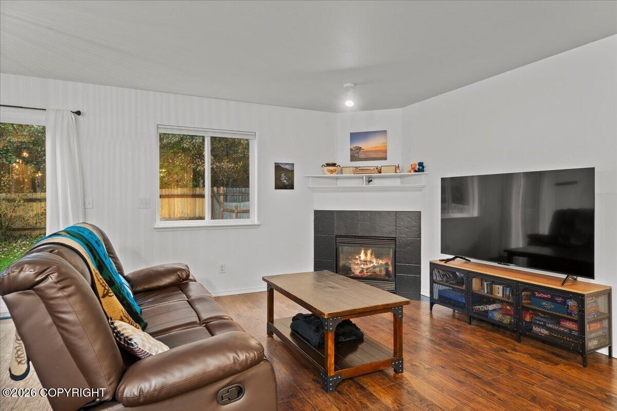 Living room with a leather reclining sofa, hardwood floors, and a lit fireplace beside a large television.