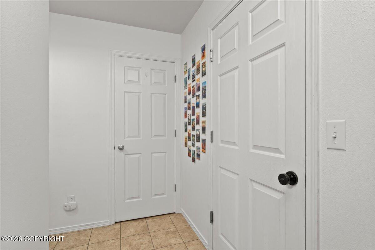 Entry hallway with tan tile floor, white paneled doors, and colorful postcards on the wall.