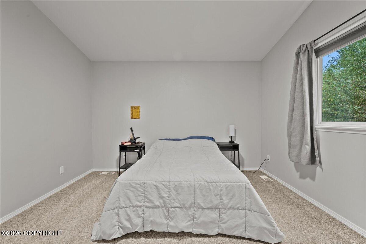 Bedroom with a centered bed, black bedside tables, beige carpet, and a window overlooking trees.