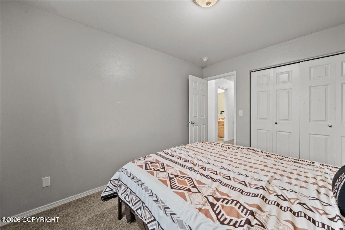 Bedroom with a geometric-patterned quilt, white paneled closet, and open bathroom doorway.