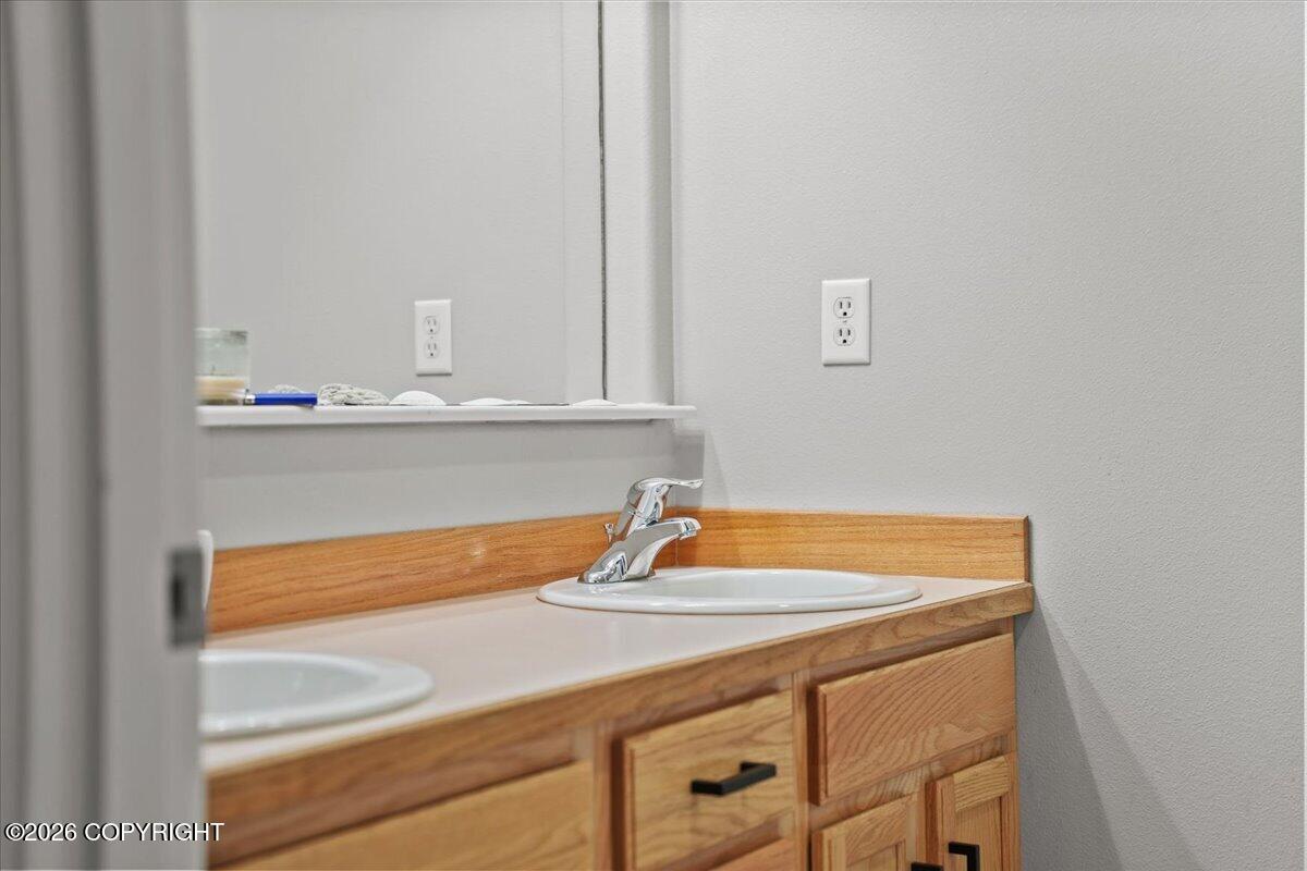 Bathroom vanity with a white countertop, chrome faucet, mirror, and honey-colored wood cabinetry.
