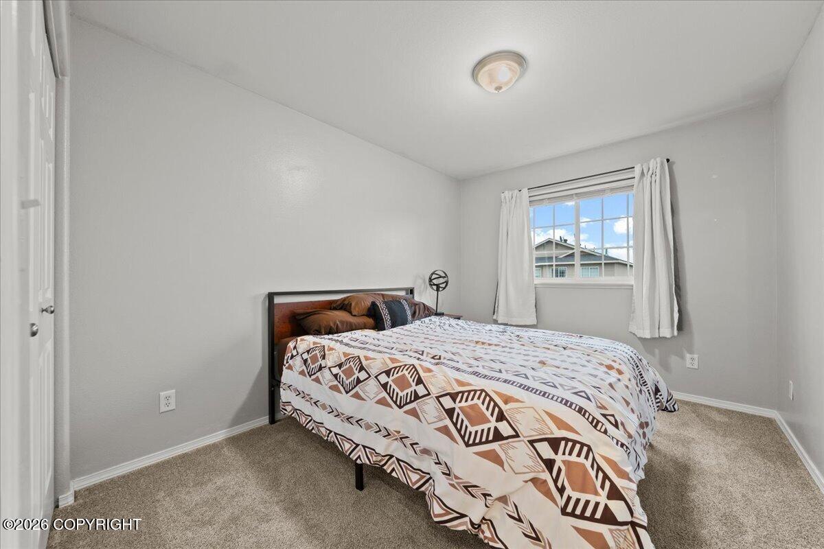 Bedroom with geometric-patterned bedding, beige carpet, and a curtained window.