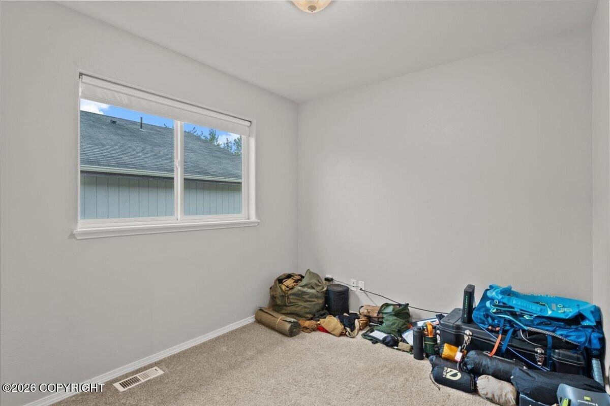 Unfurnished carpeted room with a window and outdoor gear piled along one wall.