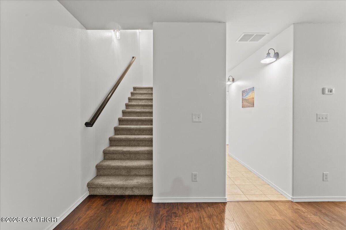 Entryway with a carpeted staircase, dark handrail, wood flooring, and tiled hallway.