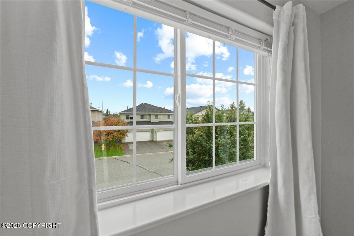 Window with white curtains overlooking neighboring homes and a tree-lined residential street.