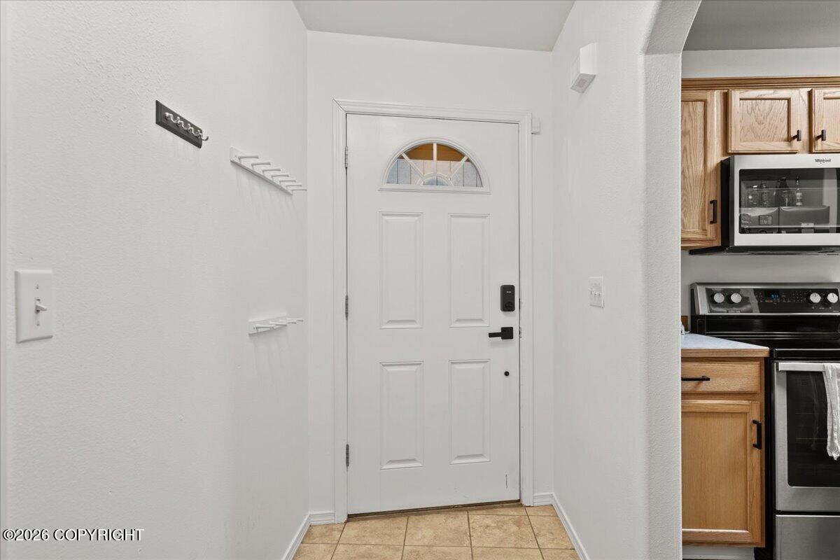 Entryway with a white front door and decorative window beside a kitchen with wood cabinets.