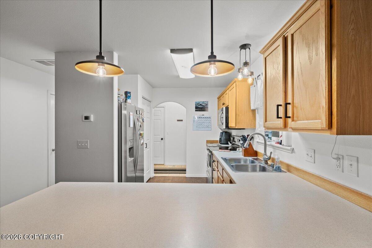 Kitchen with honey-colored wood cabinets, stainless steel refrigerator, and broad pale countertop.