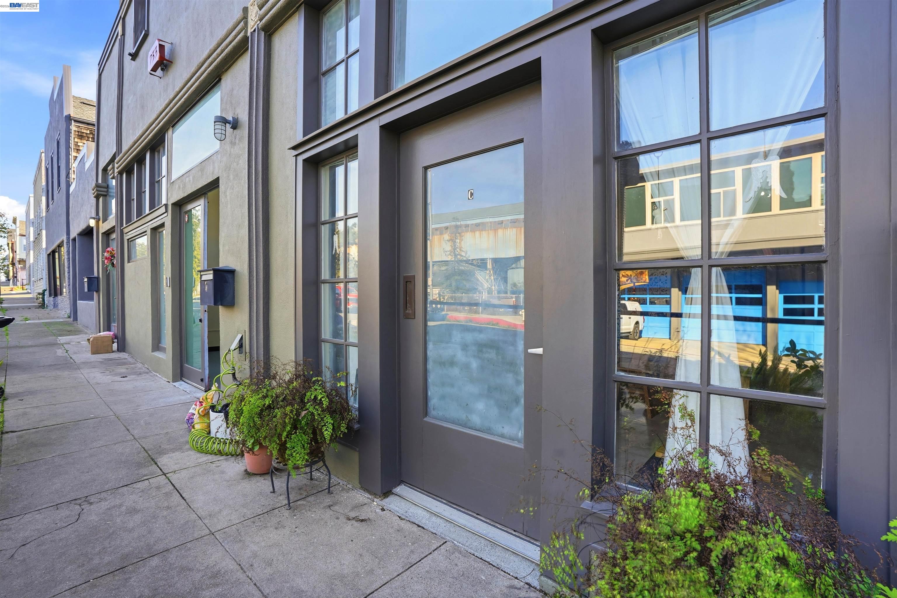 Modern gray building entrance marked C, with tall windows and potted plants along the sidewalk.