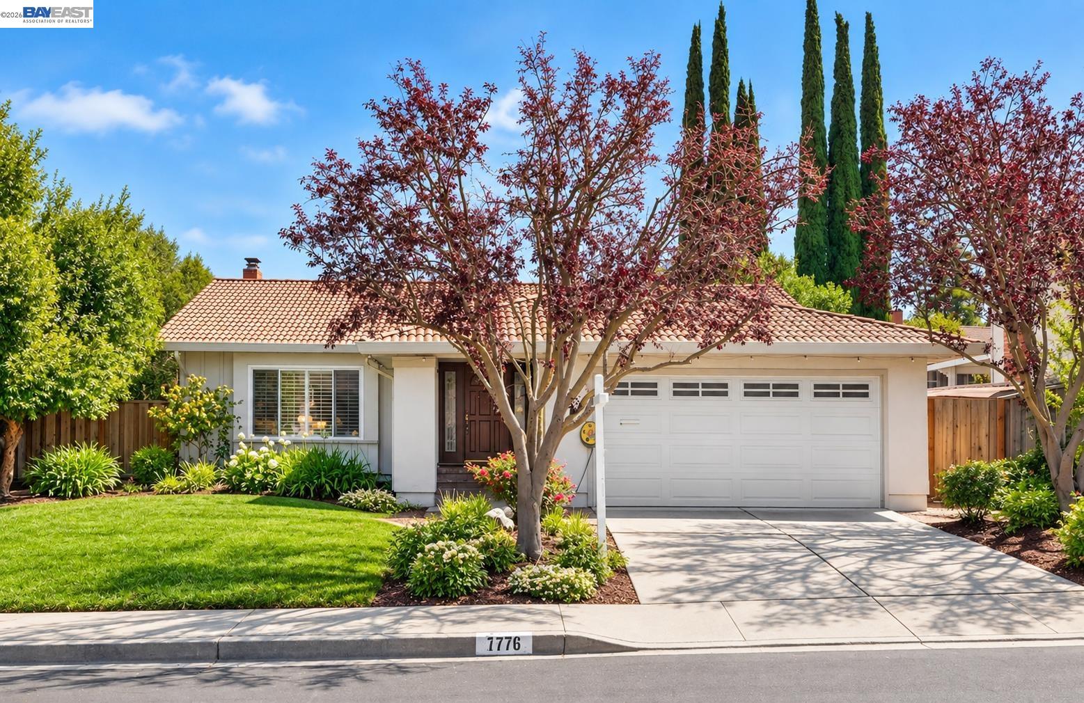Single-story home numbered 7776 with a terracotta tile roof, white garage, landscaped lawn, and mature trees.
