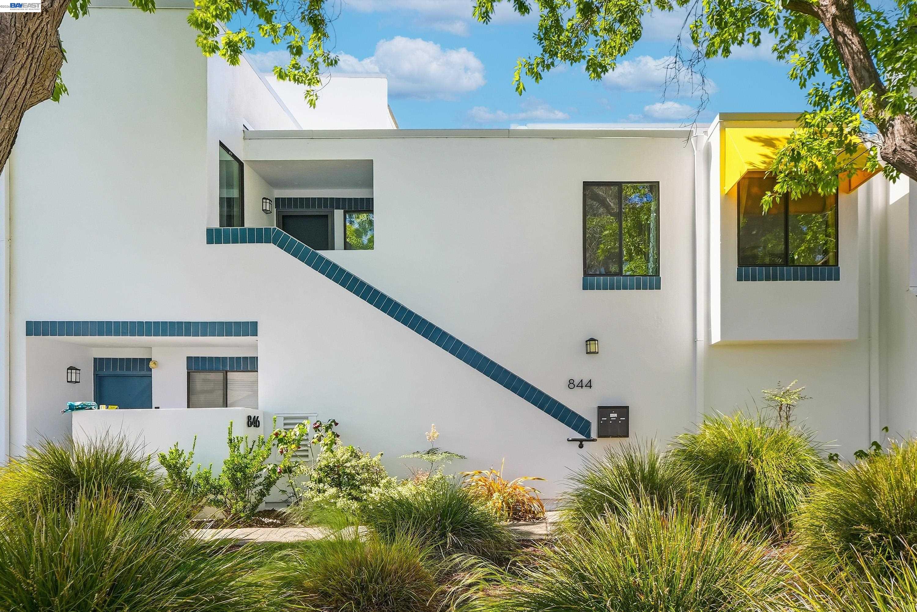 Modern white home with blue tile accents, a diagonal stair detail, and a yellow window awning.