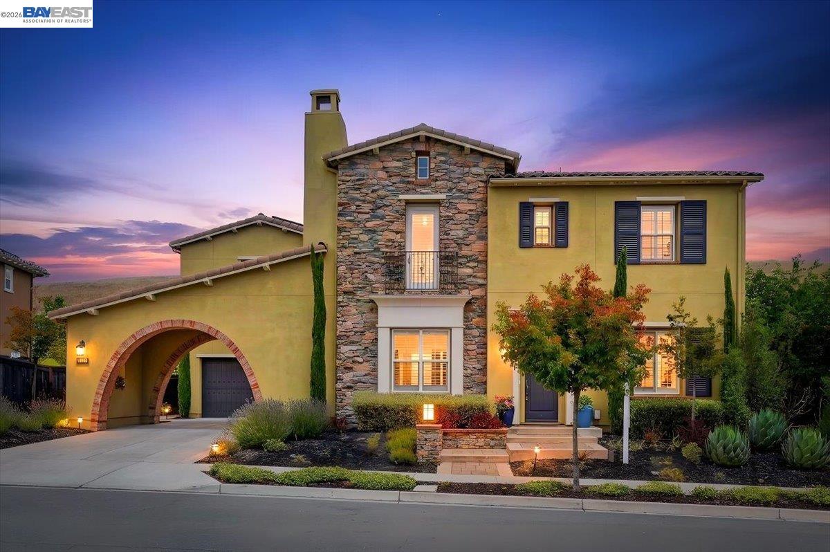 Two-story stucco home with a stone facade and arched garage entrance, photographed at dusk.