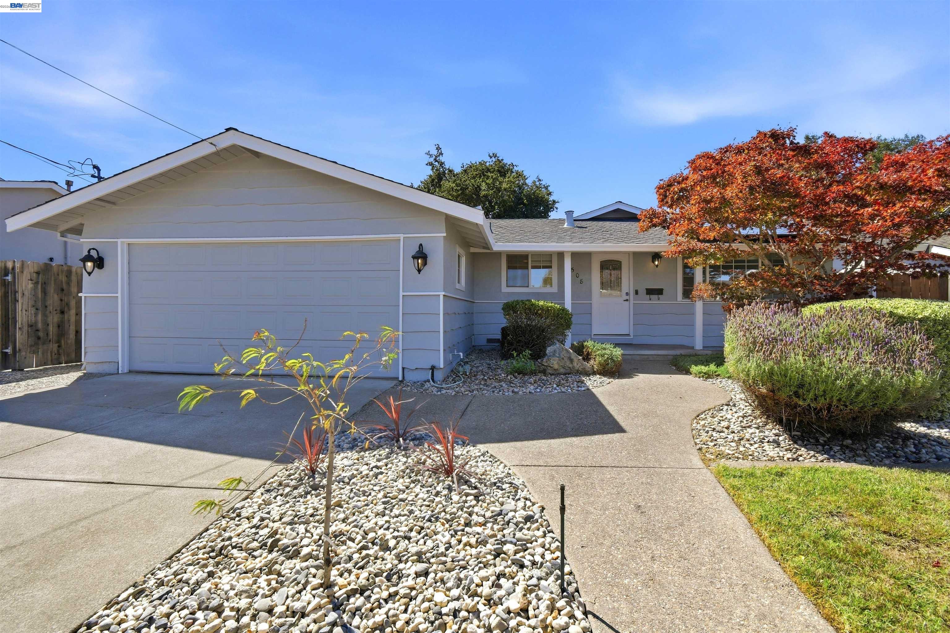 Single-story home with a double garage, rock landscaping, and a red-leaf tree by the entry.