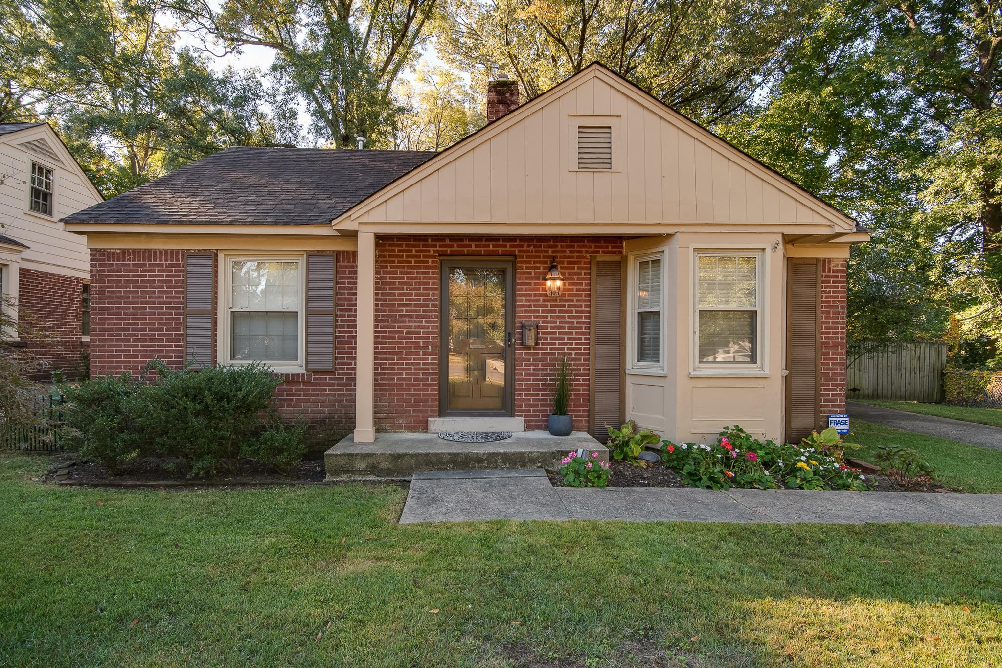 Red brick home with cream gables, a covered entry, dark shutters, and colorful flowers along the front walkway.