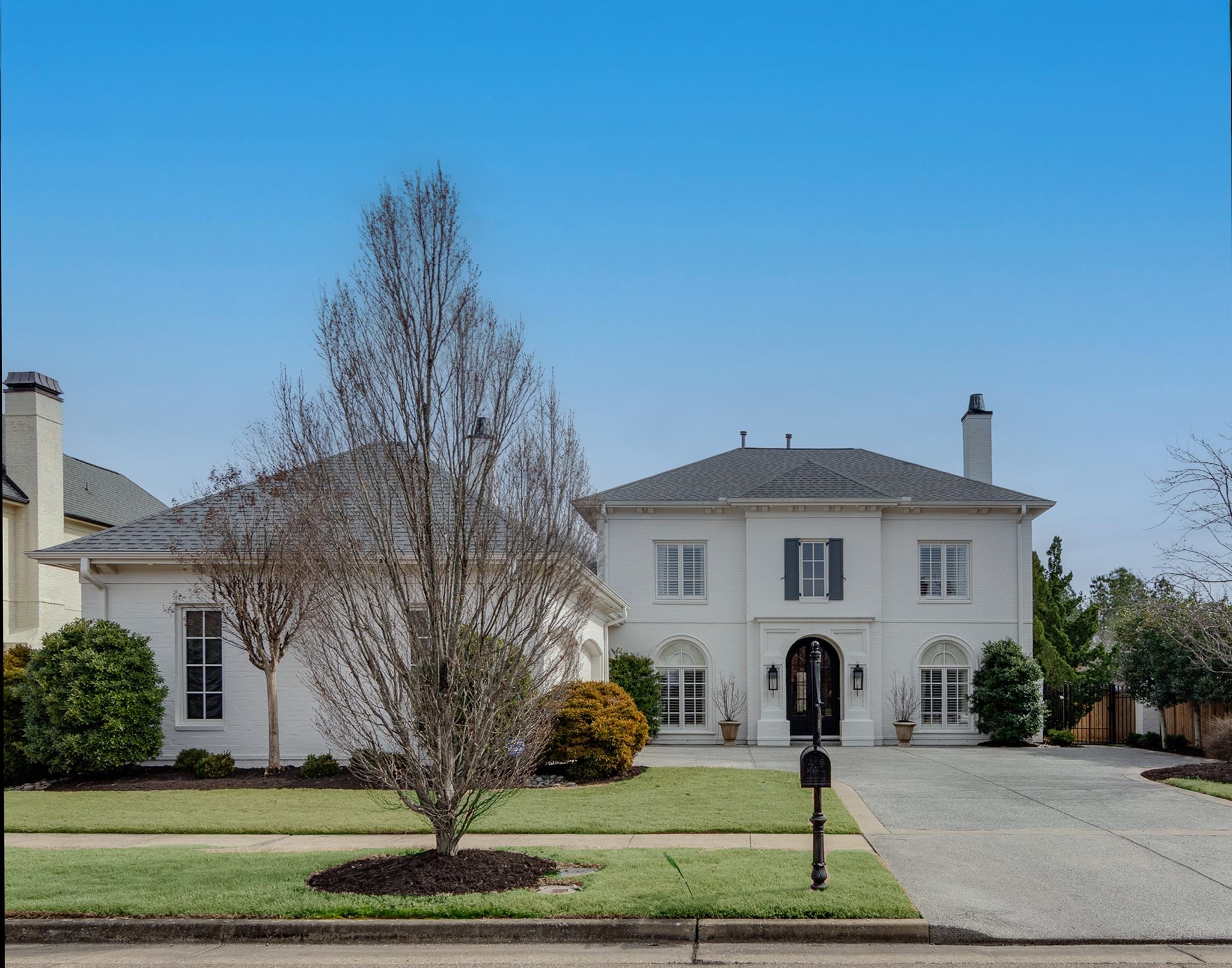 Two-story white brick home with an arched entry, broad driveway, and leafless trees in the front yard.