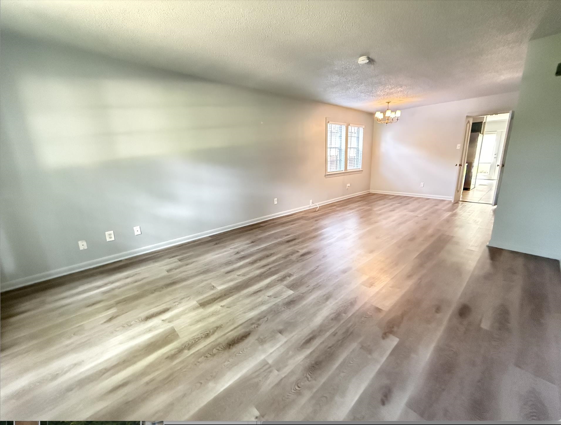 Empty living room with wood-look flooring, paired windows, and a chandelier.
