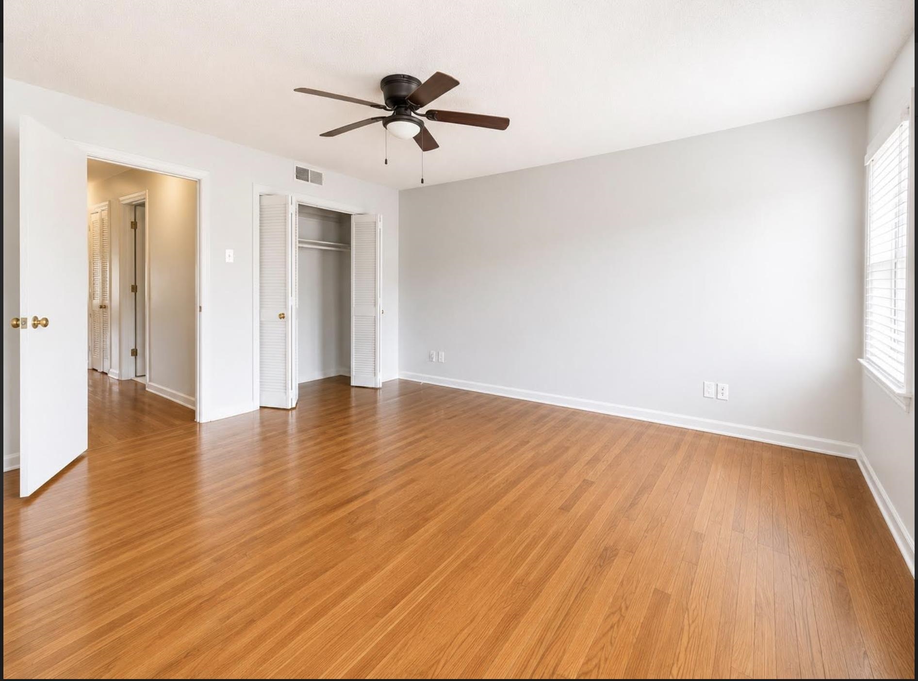 Empty bedroom with hardwood floors, a ceiling fan, and an open louvered closet.