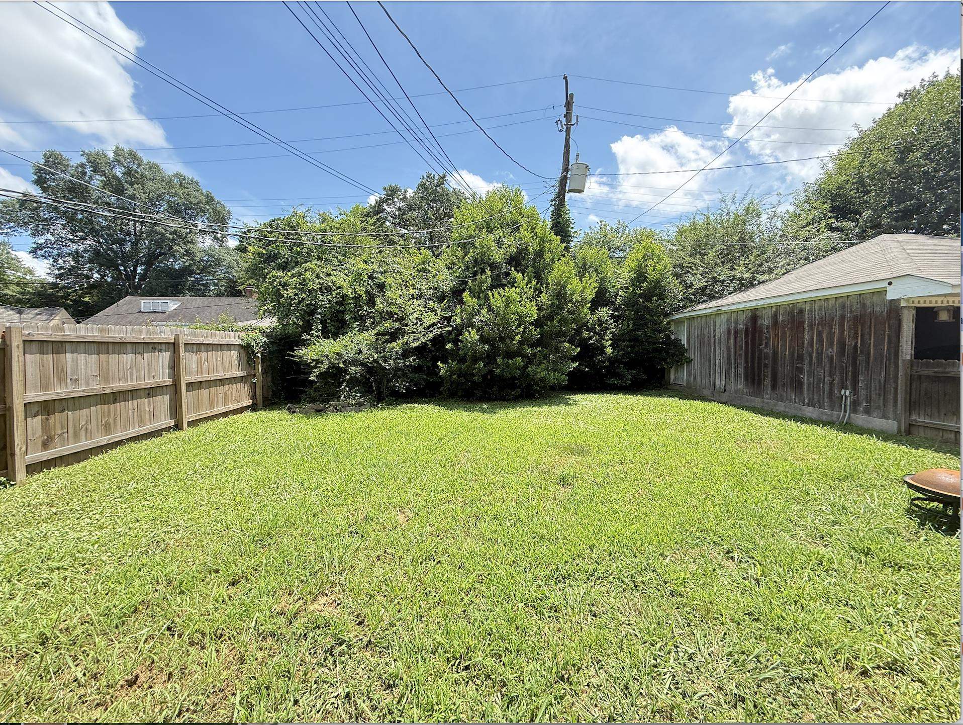 Fenced backyard with a broad lawn, dense greenery, and a wooden outbuilding.