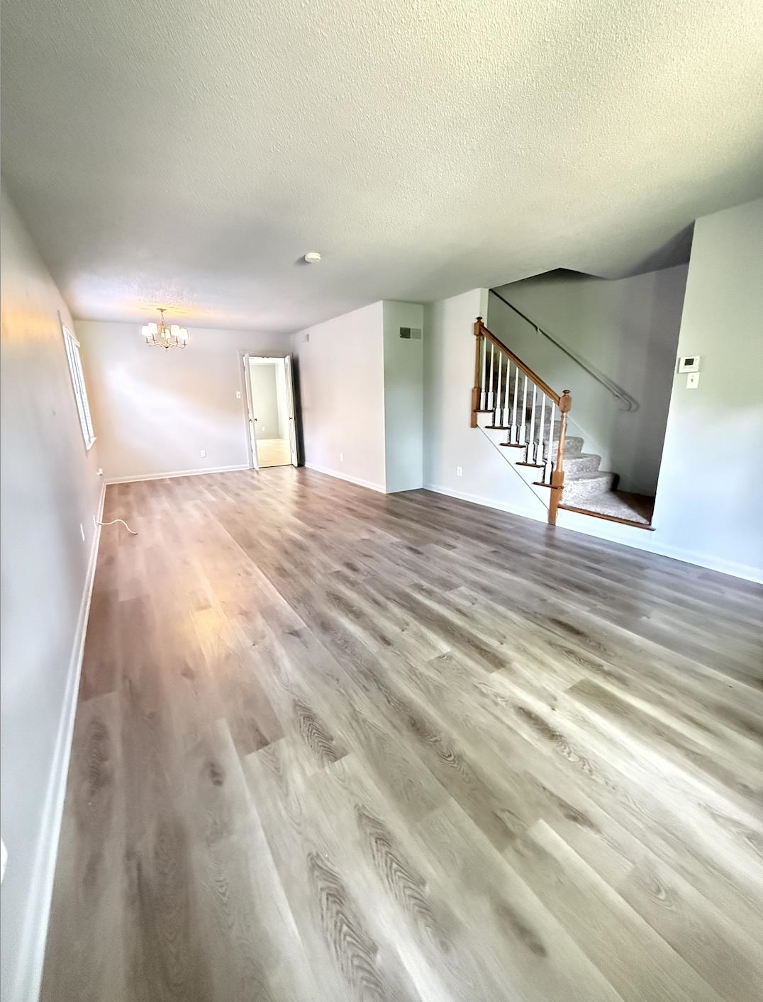 Empty living room with wood-look plank flooring and a carpeted staircase with a wooden handrail.