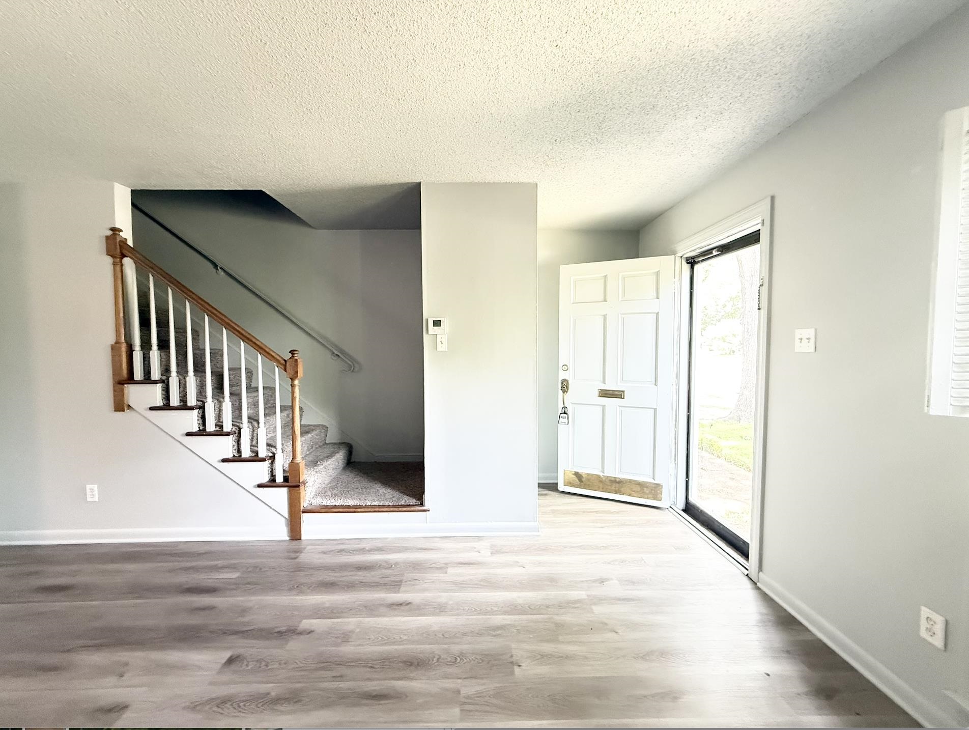 Unfurnished entryway with a carpeted staircase and an open front door.