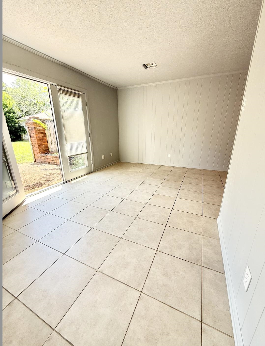 Empty tiled room with sliding glass doors opening onto a patio and yard.