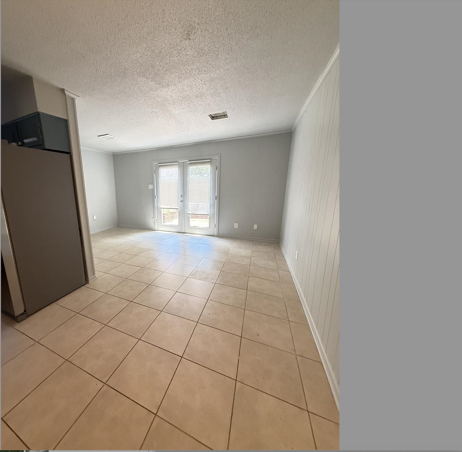 Empty tiled kitchen area with a refrigerator and double glass doors with blinds.