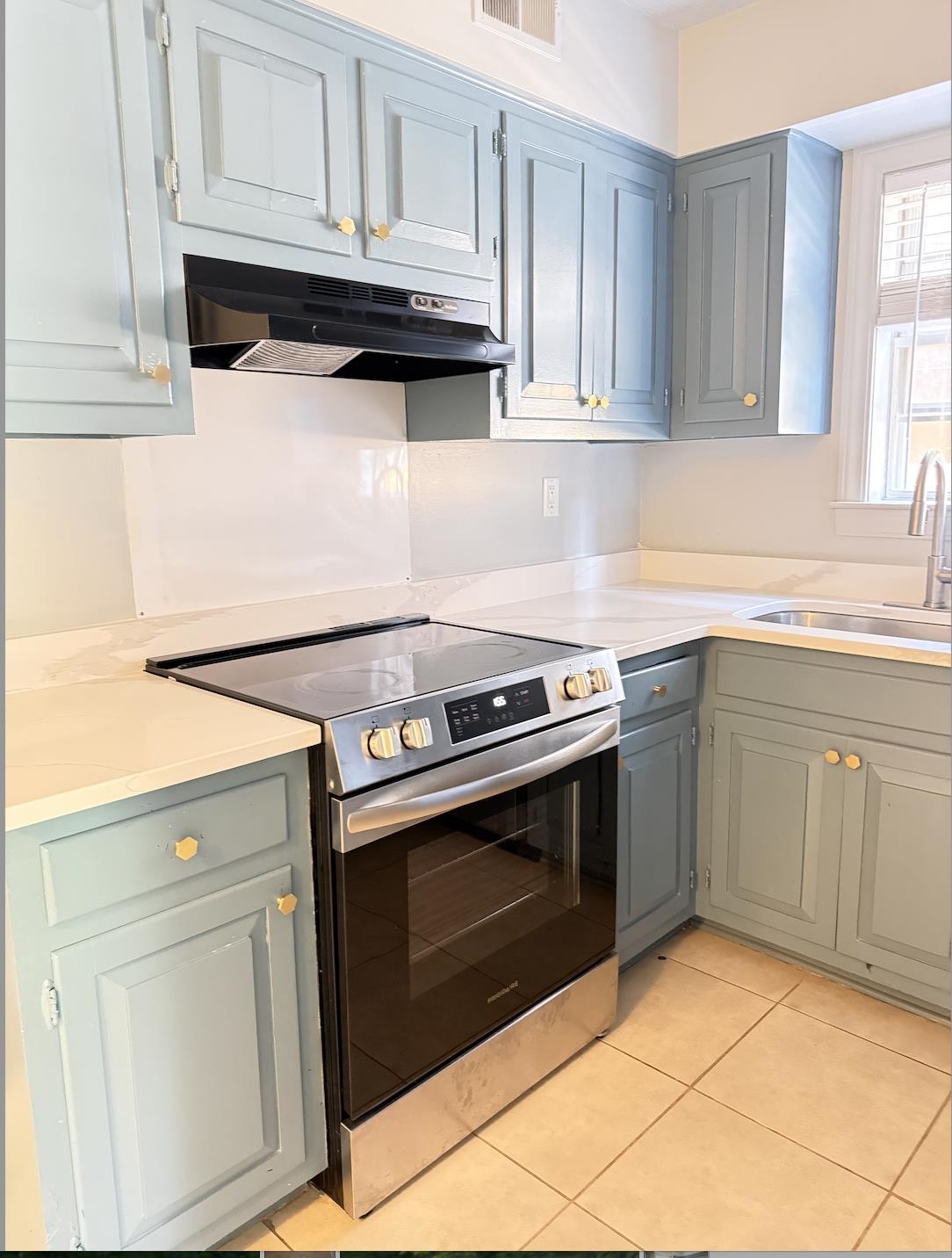 Kitchen with blue-gray cabinets, a stainless steel range, white counters, and a window-side sink.