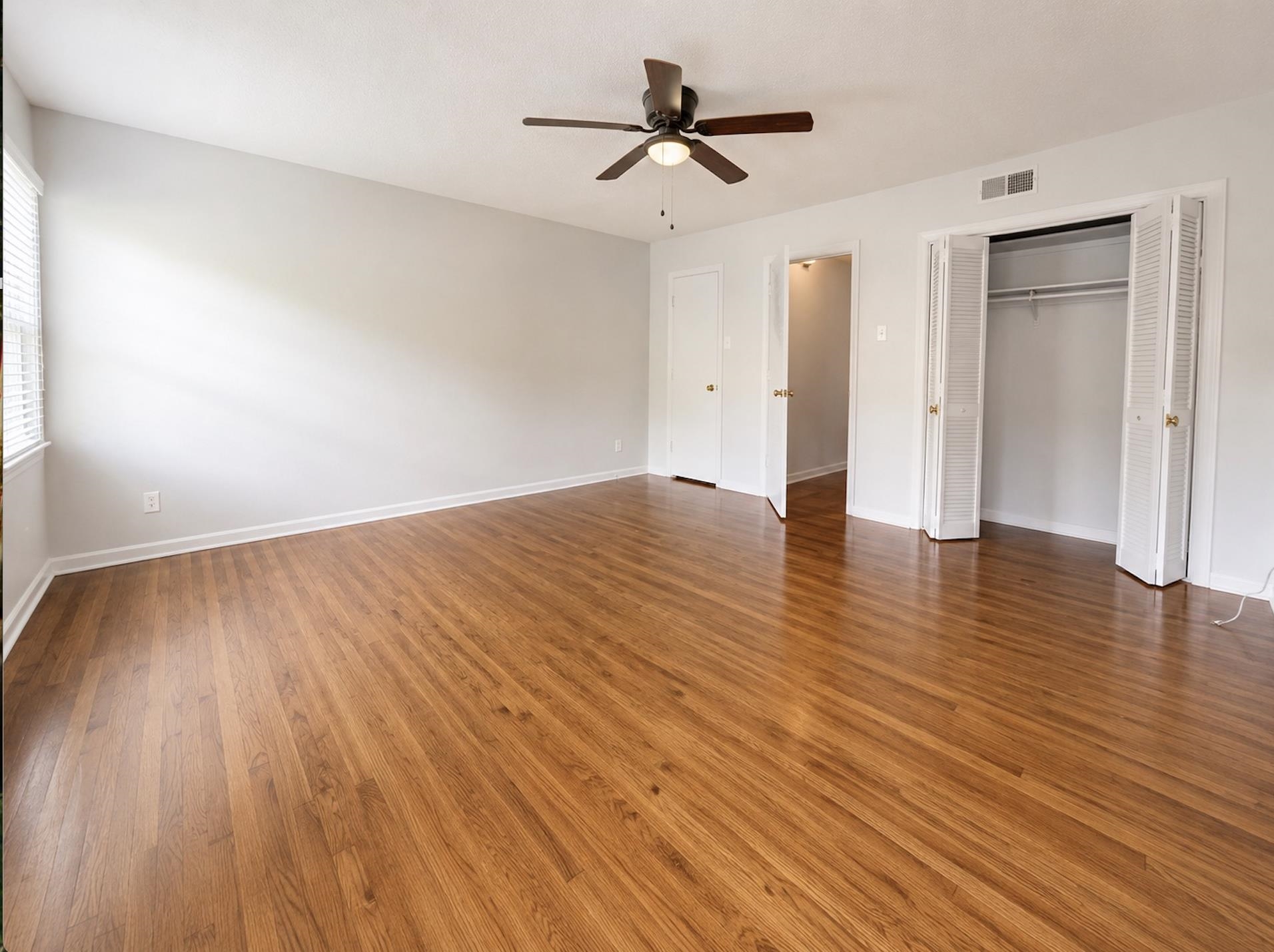 Empty bedroom with polished hardwood floors, ceiling fan, and open closet.