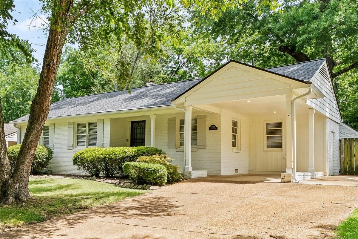 White brick house with a covered entrance and broad driveway beneath mature trees.