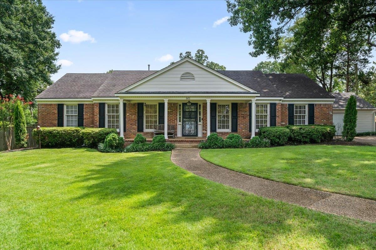 Brick ranch house with a white gabled porch, black shutters, and a curved front walkway.