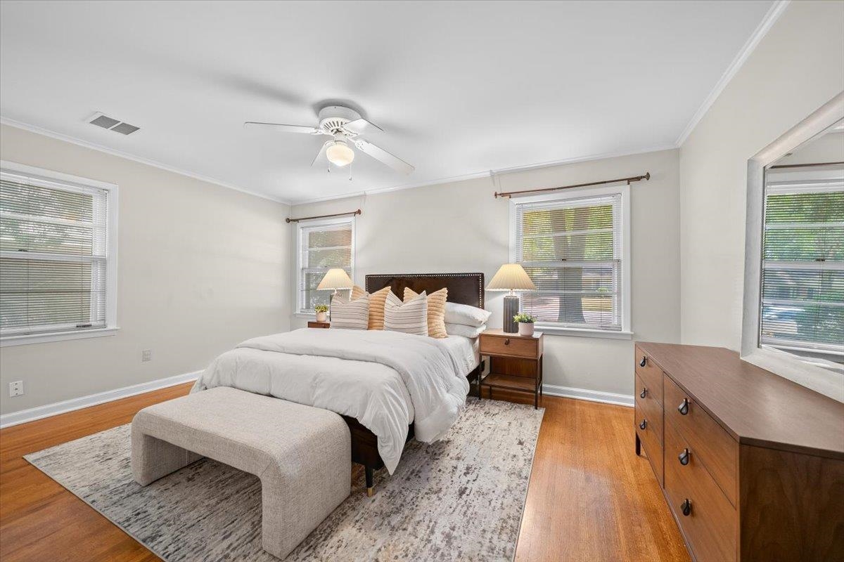 Bright bedroom with a white bed, upholstered bench, wood dresser, and hardwood floors.