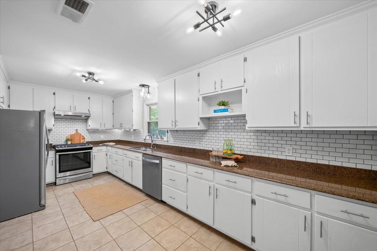 Kitchen with white cabinets, brown countertops, subway tile backsplash, and stainless steel appliances.