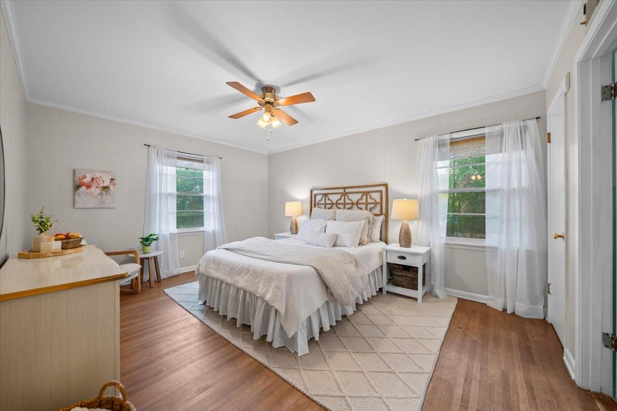 Staged bedroom with a white bed, geometric headboard, sheer curtains, and hardwood floors.